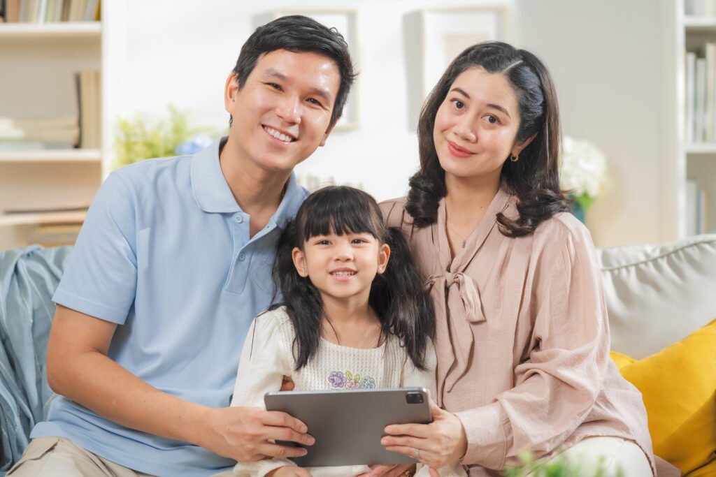 A family of three smiles together while holding a tablet.