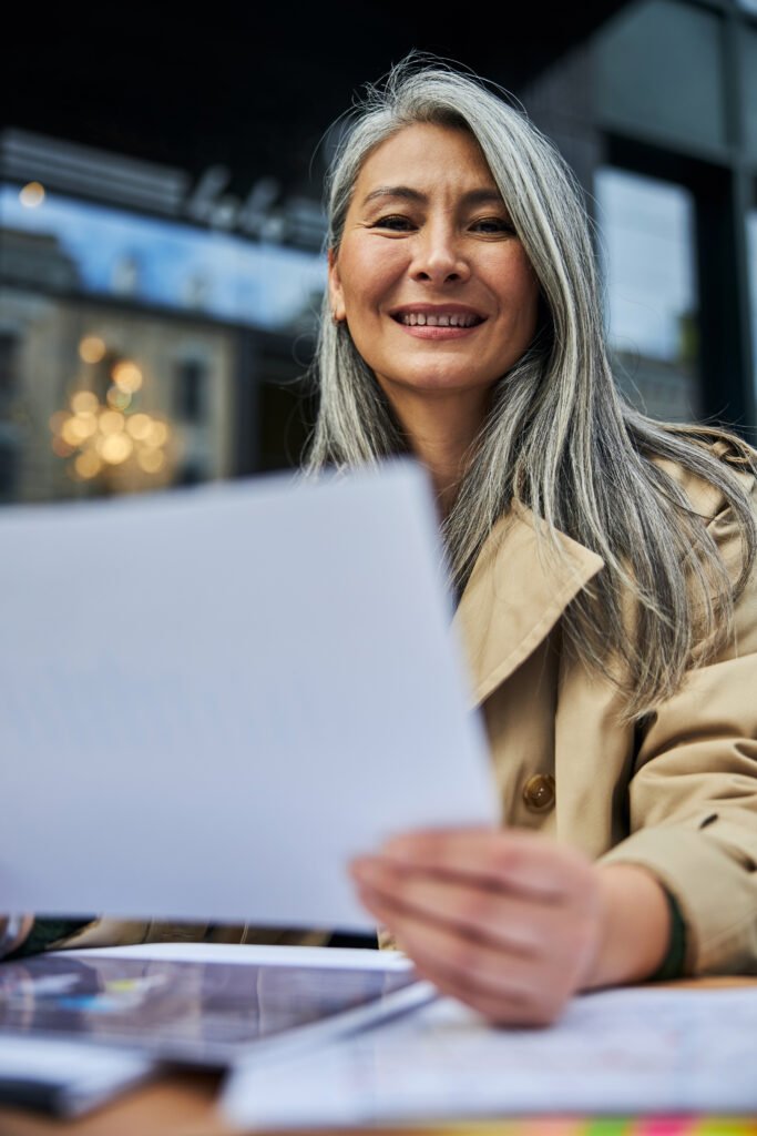 A mature woman with long gray hair smiles while looking at a document.